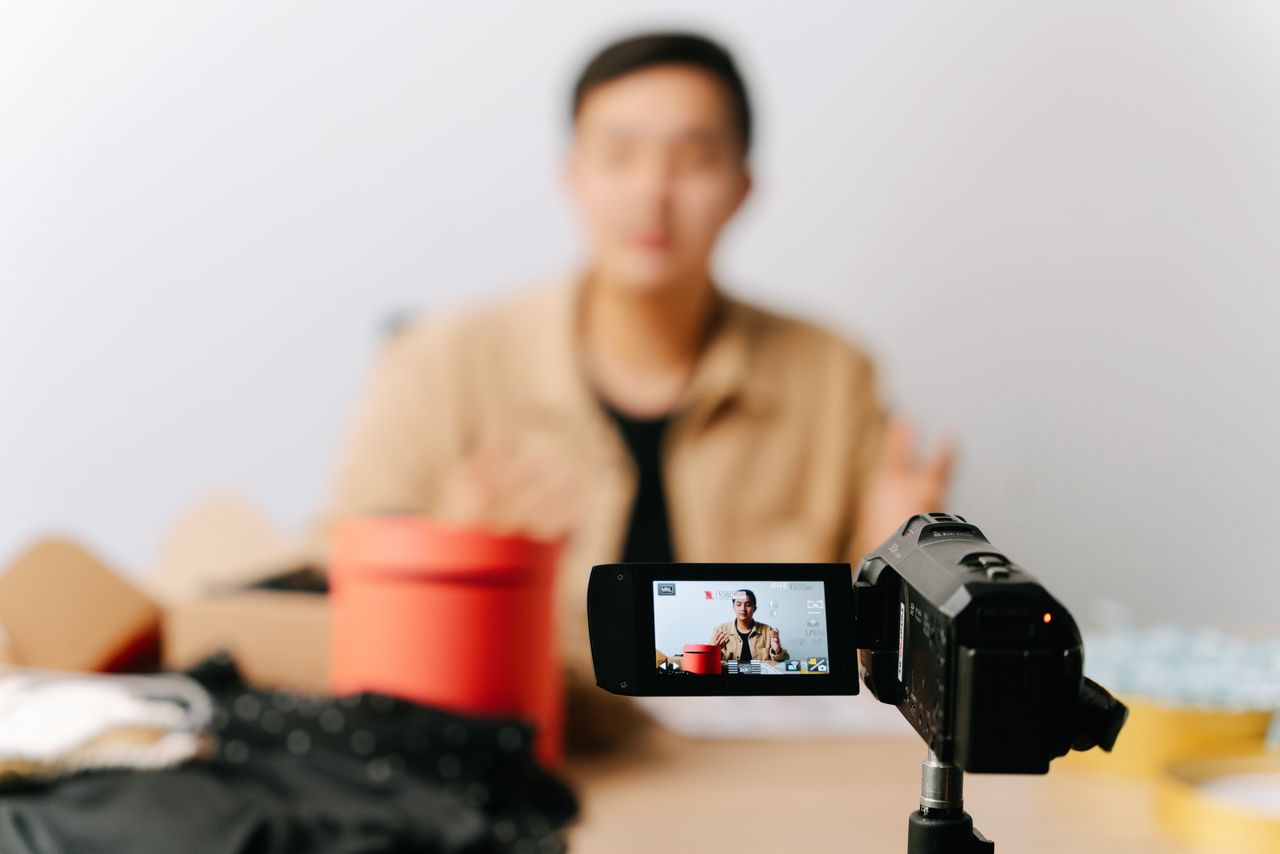A blogger is seated indoors in front of a camera while recording a video.